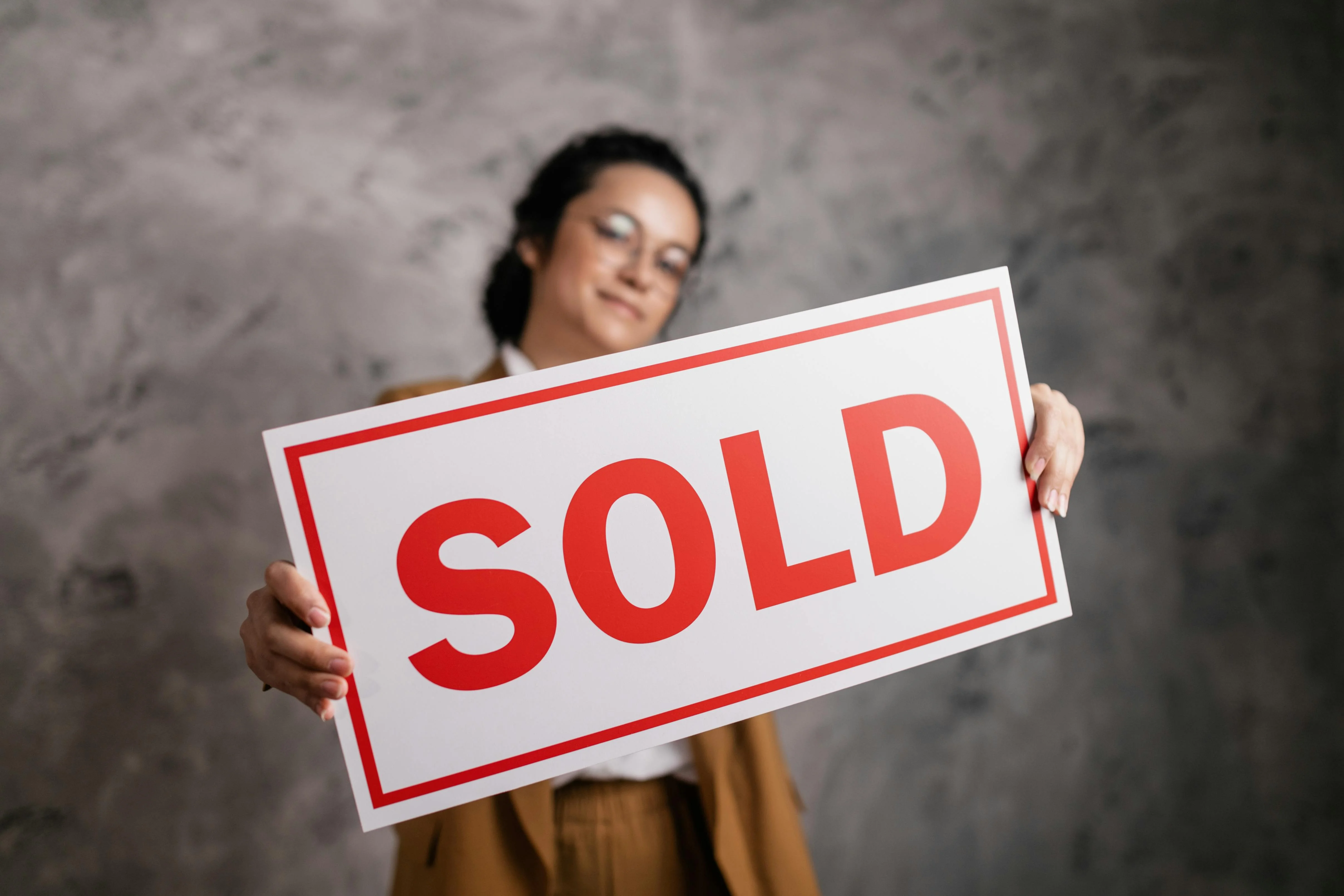 Agent standing in front of a sold sign holding a phone showing a link-in-bio page